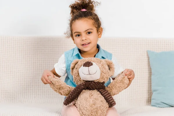 Beautiful happy african american child holding teddy bear and smiling at camera — Stock Photo