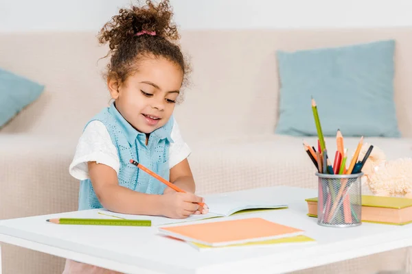 Adorable sonriente afroamericano niño estudiando y escribiendo con lápiz - foto de stock