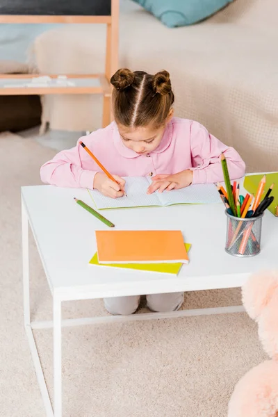 Vista ad alto angolo di bambino carino che scrive a matita mentre studia a casa — Foto stock