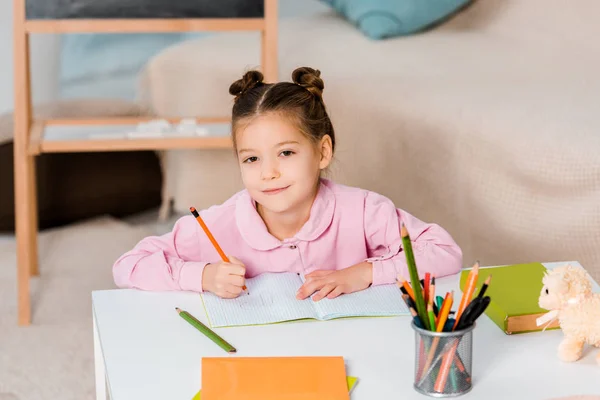 Vista de ángulo alto de adorable dibujo infantil con lápiz y sonriendo a la cámara - foto de stock