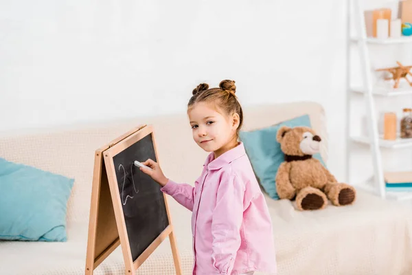 Adorable child drawing on chalkboard and smiling at camera — Stock Photo