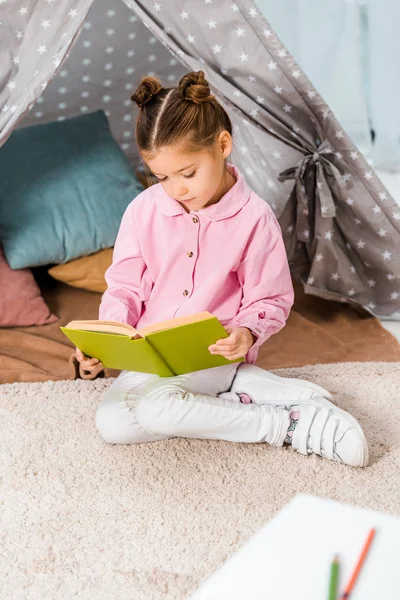 Adorable child sitting on carpet and reading book — Stock Photo