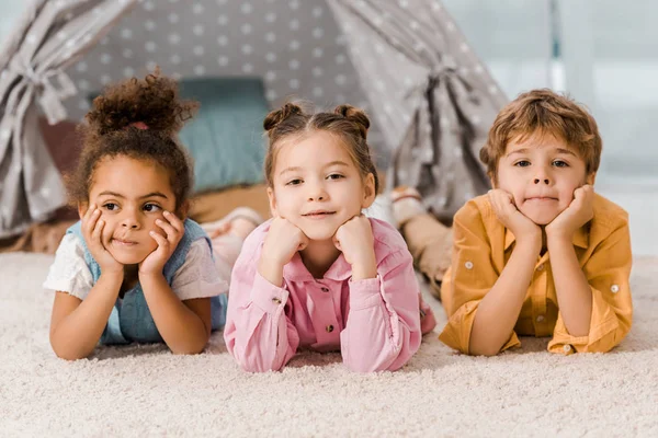 Чарівні багатонаціональні діти лежать на килимі і дивляться на камеру — стокове фото