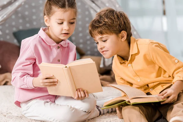 Entzückende Kinder sitzen auf Teppich und lesen gemeinsam Bücher — Stockfoto