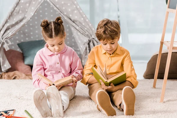 Schöne Kinder sitzen auf Teppich und lesen gemeinsam Bücher — Stockfoto