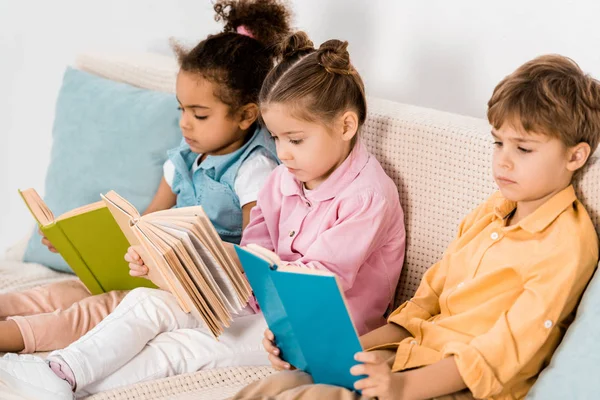 Очаровательные многонациональные дети, сидящие на диване и читающие книги — стоковое фото