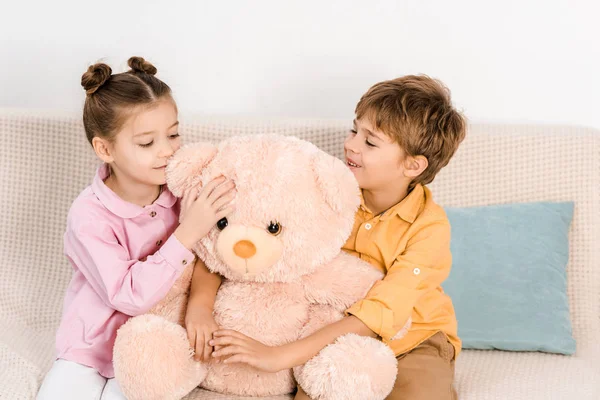 Beaux enfants heureux assis avec ours en peluche rose sur le canapé — Photo de stock