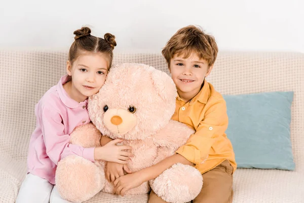 Adorables enfants heureux étreignant ours en peluche rose et souriant à la caméra — Photo de stock