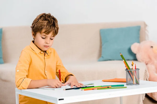 Ragazzo concentrato che scrive con la penna e studia a tavola a casa — Foto stock