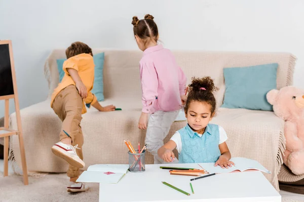 Vista de ángulo alto de adorables niños multiétnicos jugando y dibujando juntos - foto de stock