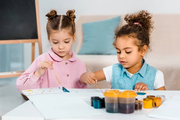 Lindo poco multiétnico niños sentado y pintura juntos - foto de stock