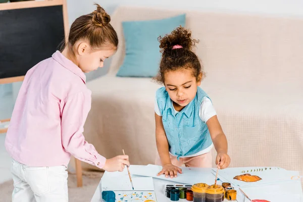 Schöne multiethnische Kinder malen mit Farben und Pinseln zusammen — Stockfoto