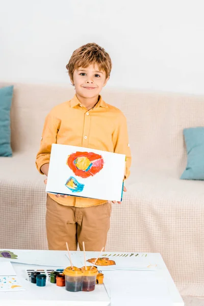 Adorável menino feliz segurando foto e sorrindo para a câmera — Fotografia de Stock