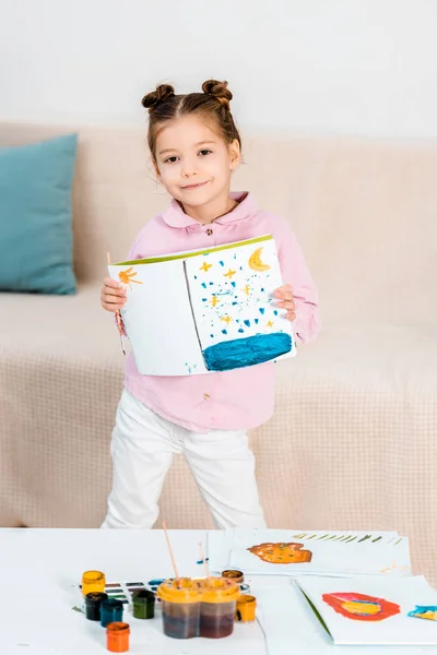 Cute happy child holding picture and smiling at camera — Stock Photo