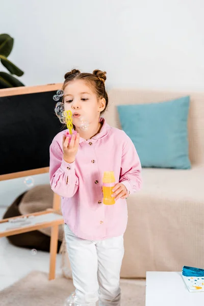 Beautiful child standing near blackboard and blowing soap bubbles — Stock Photo