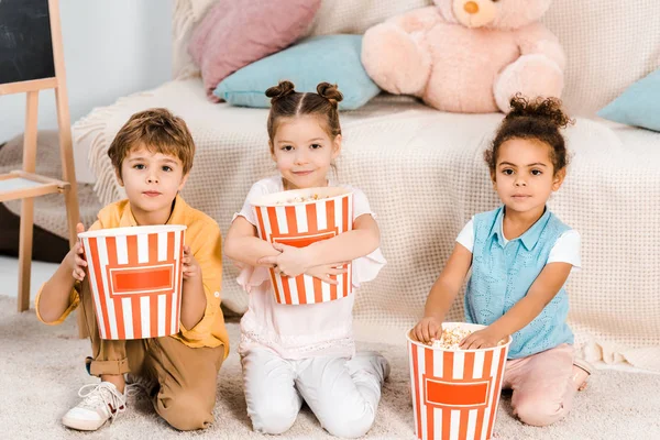 Очаровательные мультиэтнические дети держат коробки с попкорном и смотрят в камеру — стоковое фото