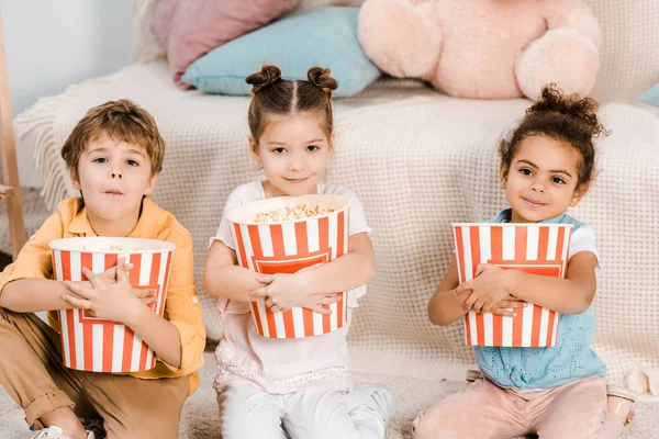 Adorables niños pequeños sosteniendo cajas con palomitas de maíz y sonriendo a la cámara - foto de stock