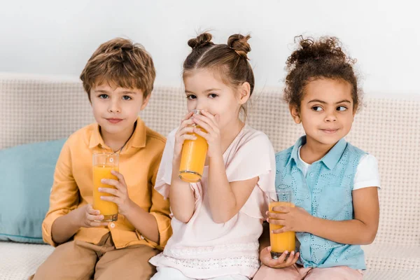 Adorables niños multiétnicos sentados juntos y bebiendo jugo - foto de stock