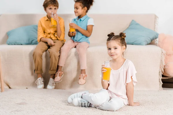 Adorables niños multiétnicos bebiendo jugo de naranja de vasos - foto de stock
