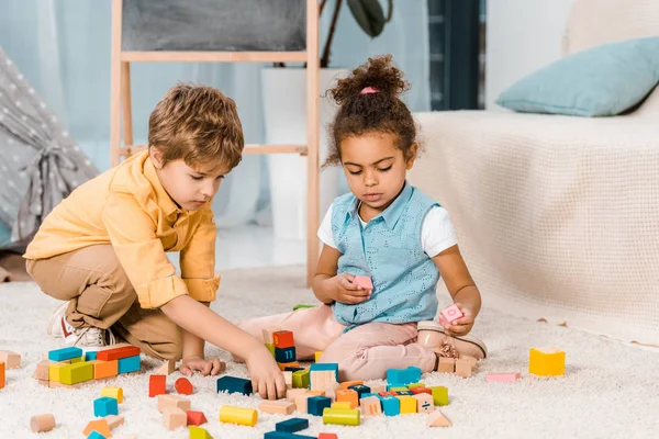 Entzückende multiethnische Kinder, die mit bunten Holzklötzen auf Teppich spielen — Stockfoto