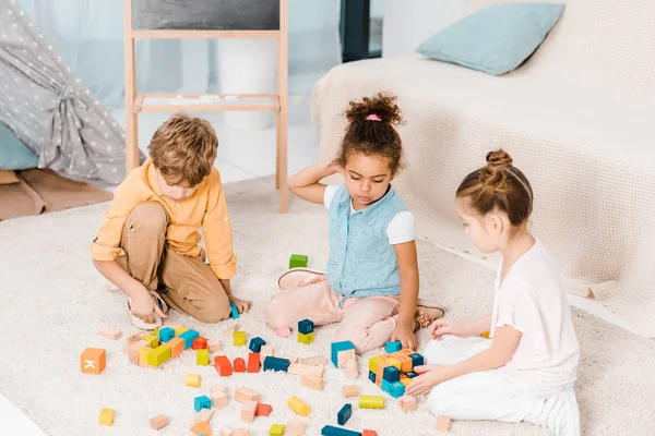 Blick aus der Vogelperspektive auf entzückende multiethnische Kinder, die mit bunten Würfeln auf Teppich spielen — Stockfoto