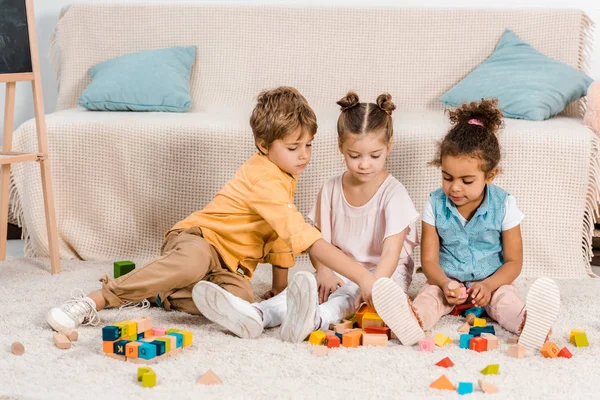 Adorables pequeños niños étnicos jugando con cubos de colores en la alfombra - foto de stock
