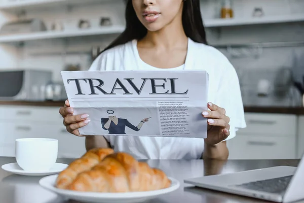 Imagen recortada de chica de raza mixta en bata blanca leyendo periódico de viaje en la mañana en la cocina - foto de stock