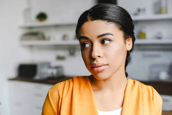 Retrato de bela menina de raça mista em camisa laranja olhando para longe na cozinha — Fotografia de Stock