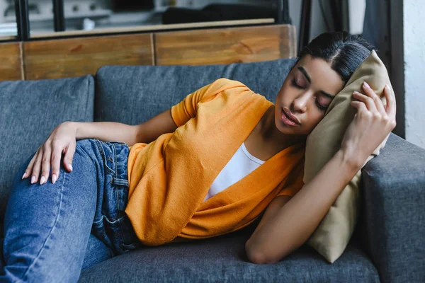 Красивая девушка смешанной расы в оранжевой рубашке и джинсах спит на диване дома — стоковое фото