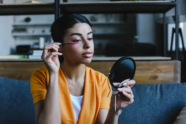 Bela menina de raça mista em camisa laranja aplicando rímel em casa — Fotografia de Stock