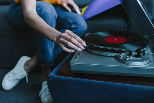 Cropped image of mixed race girl turning on gramophone with retro vinyl at home — Stock Photo