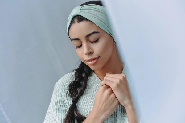 Attractive mixed race girl in turquoise sweater and headband standing with closed eyes at home — Stock Photo