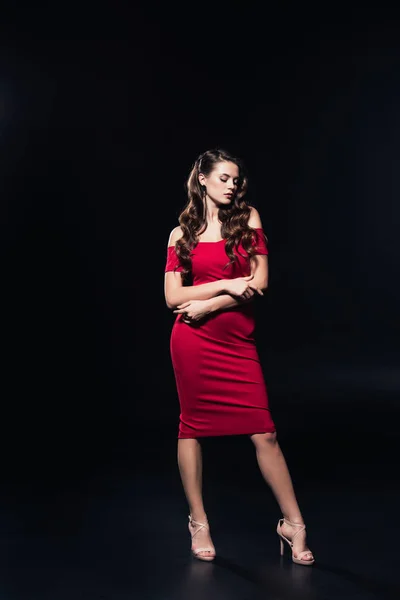 Attractive woman in red dress posing with arms crossed isolated on black — Stock Photo