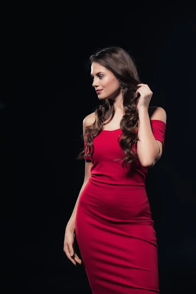 Schöne Frau in rotem Kleid, die Haare berührt, posiert und wegschaut, isoliert auf schwarz — Stockfoto