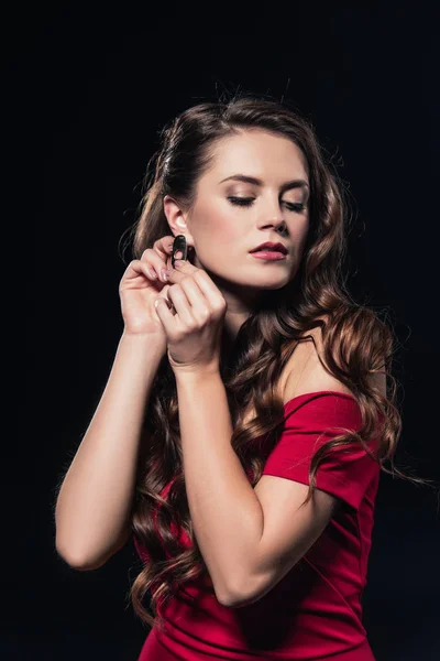 Woman in red dress putting on earring isolated on black — Stock Photo