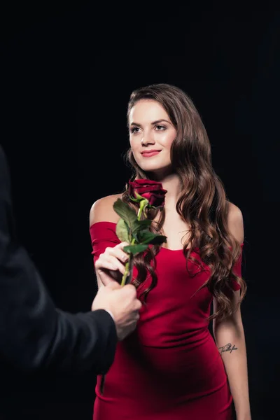Homme présentant rose à belle femme souriante en robe rouge isolé sur noir — Photo de stock