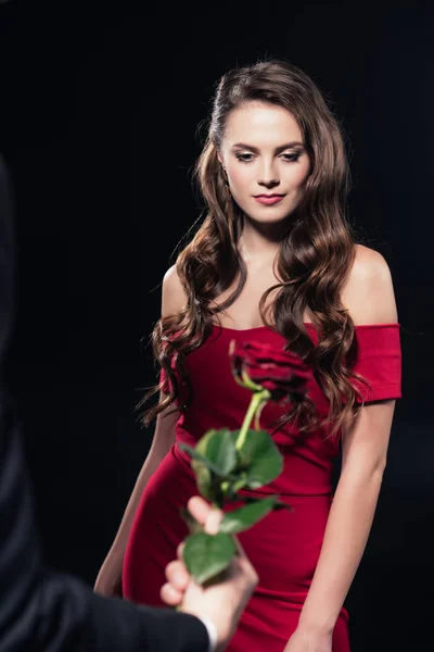 Hombre presentando rosa a mujer en vestido rojo aislado en negro - foto de stock