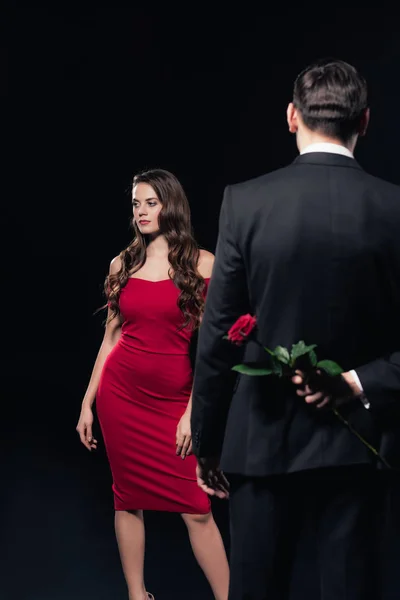 Hombre escondido se levantó detrás de la espalda con la mujer en vestido rojo sobre fondo aislado en negro - foto de stock
