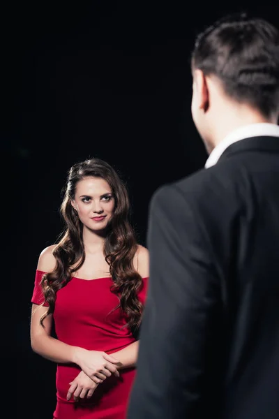 Selektiver Fokus der schönen Frau in rotem Kleid mit Mann im Vordergrund isoliert auf schwarz — Stockfoto