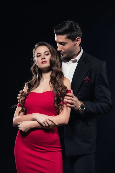 Man embracing attractive woman in red dress isolated on black — Stock Photo