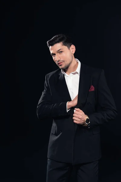 Handsome man posing in in suit and looking at camera isolated on black — Stock Photo