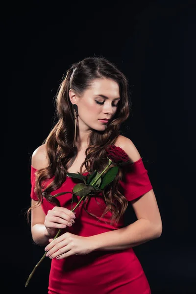 Femme avec les yeux fermés en robe rouge tenant rose isolé sur noir — Photo de stock