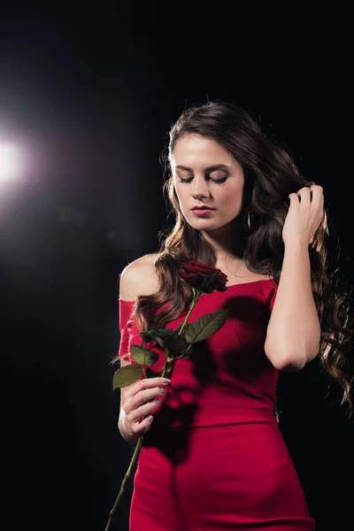 Жінка в червоній сукні з закритими очима тримає троянду на чорному тлі — стокове фото