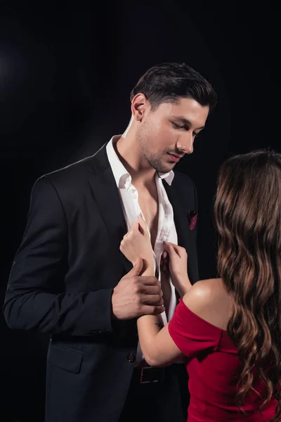 Woman in red dress undressing handsome man isolated on black — Stock Photo