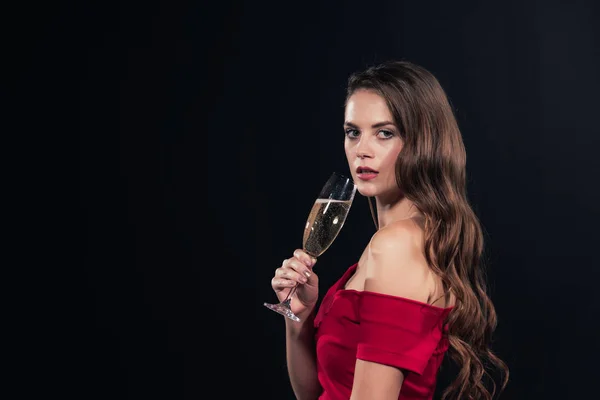 Beautiful woman in red dress looking at camera and holding glass of champagne isolated on black — Stock Photo
