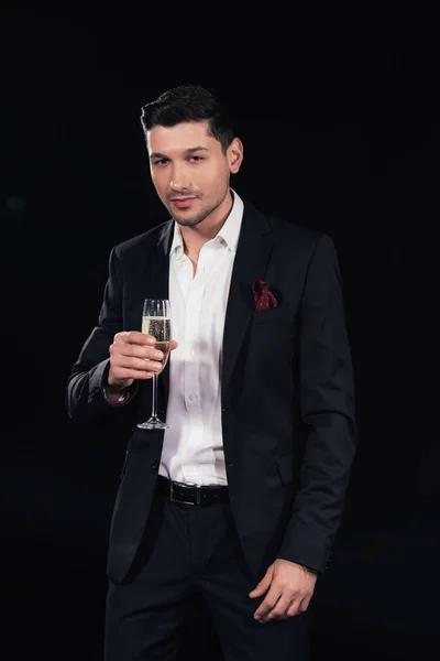 Hombre guapo mirando a la cámara y sosteniendo la copa de champán aislado en negro - foto de stock
