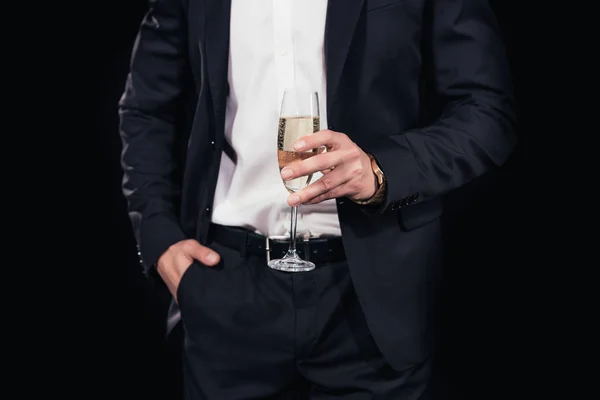 Vue recadrée de l'homme en costume avec la main dans la poche tenant verre de champagne isolé sur noir — Photo de stock