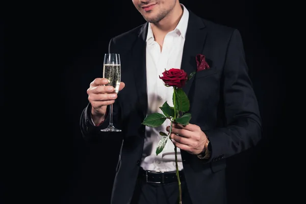 Cropped view of man holding glass of champagne and red rose isolated on black — Stock Photo