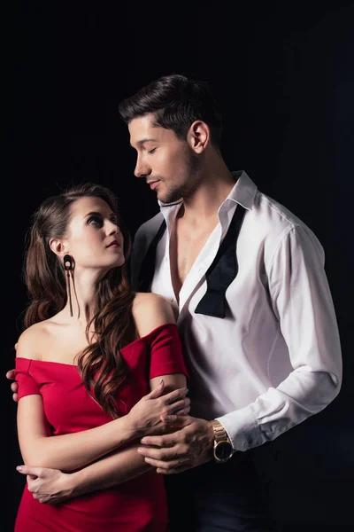 Hombre abrazando hermosa mujer en vestido rojo aislado en negro - foto de stock