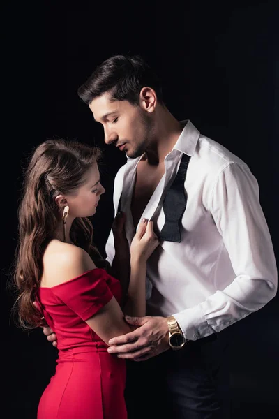 Woman in red dress undressing man shirt isolated on black — Stock Photo